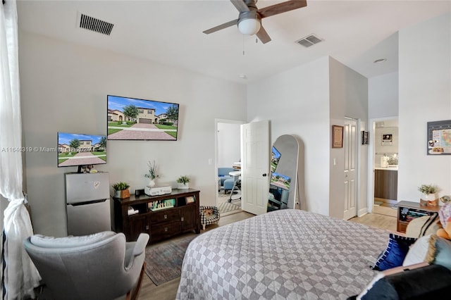 bedroom featuring light hardwood / wood-style flooring, ceiling fan, stainless steel refrigerator, and connected bathroom