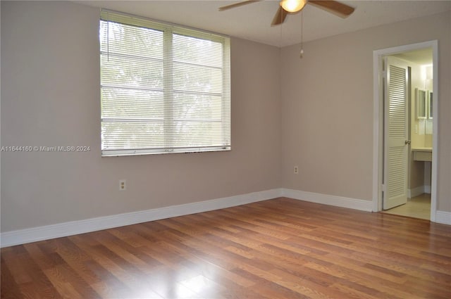 unfurnished bedroom with ceiling fan, ensuite bath, wood-type flooring, and multiple windows