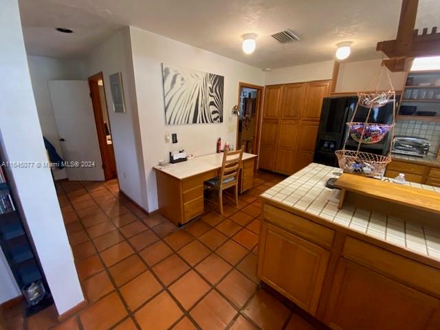 kitchen with tile countertops, black refrigerator, pendant lighting, and tile patterned floors