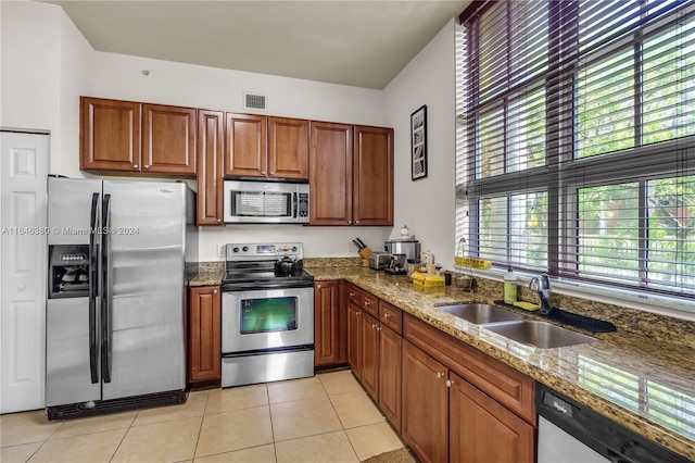 kitchen featuring light tile patterned floors, a sink, appliances with stainless steel finishes, brown cabinetry, and dark stone countertops