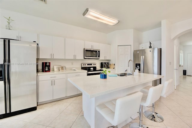 kitchen featuring light countertops, appliances with stainless steel finishes, light tile patterned flooring, white cabinetry, and an island with sink