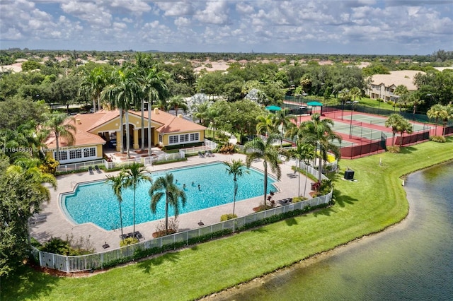 community pool with a water view, a tennis court, fence, and a yard