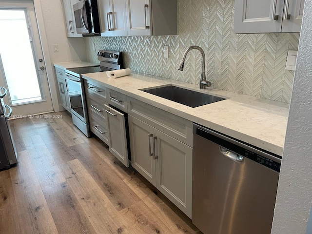 kitchen featuring sink, light hardwood / wood-style flooring, gray cabinets, stainless steel appliances, and decorative backsplash