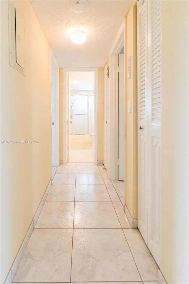 corridor featuring a textured ceiling, light tile patterned flooring, and electric panel