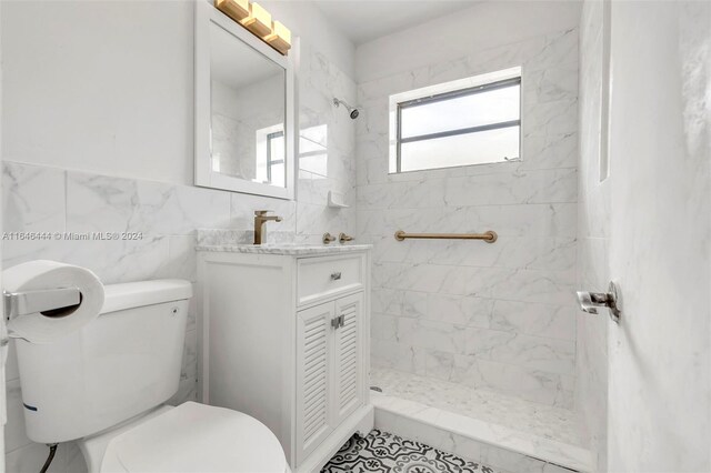 bathroom featuring vanity, tile patterned flooring, a tile shower, tile walls, and toilet