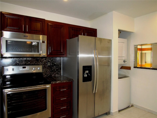 kitchen featuring decorative backsplash, dark stone counters, stacked washer / drying machine, appliances with stainless steel finishes, and light tile patterned flooring