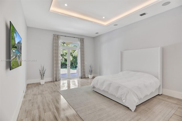 bedroom featuring light hardwood / wood-style floors, a raised ceiling, access to outside, and french doors