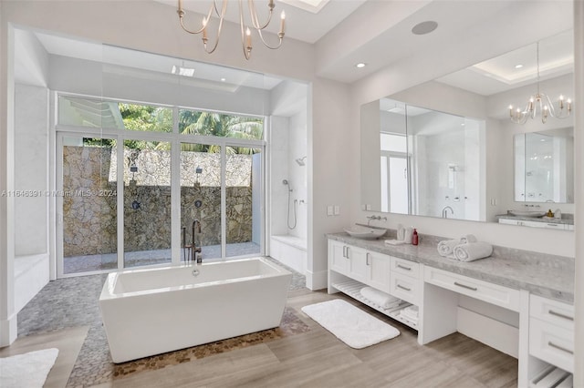 bathroom featuring a notable chandelier, a bathtub, vanity, and a tray ceiling