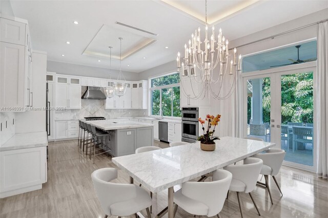 dining room with sink, a notable chandelier, french doors, light hardwood / wood-style floors, and a tray ceiling