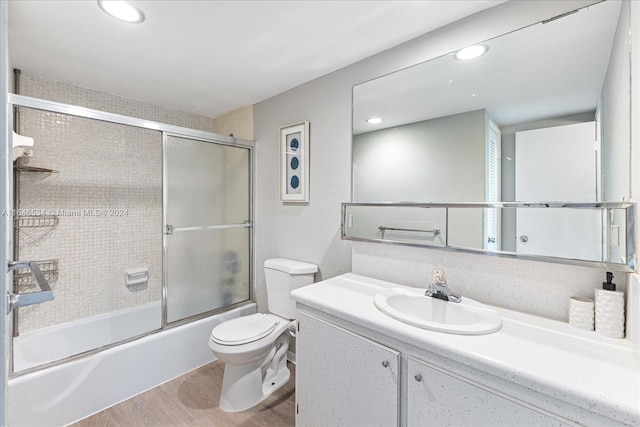 full bathroom with bath / shower combo with glass door, vanity, hardwood / wood-style floors, and toilet