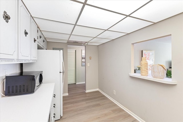 kitchen with light wood-type flooring, a drop ceiling, white refrigerator, and white cabinets