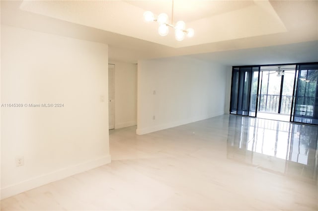 unfurnished room with ceiling fan with notable chandelier, a raised ceiling, and expansive windows