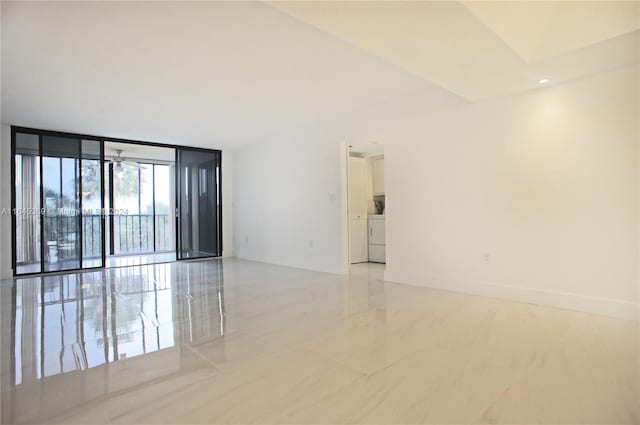 unfurnished room with washer / clothes dryer, ceiling fan, and a wall of windows