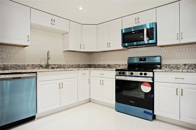 kitchen with light stone countertops, backsplash, stainless steel appliances, and white cabinets