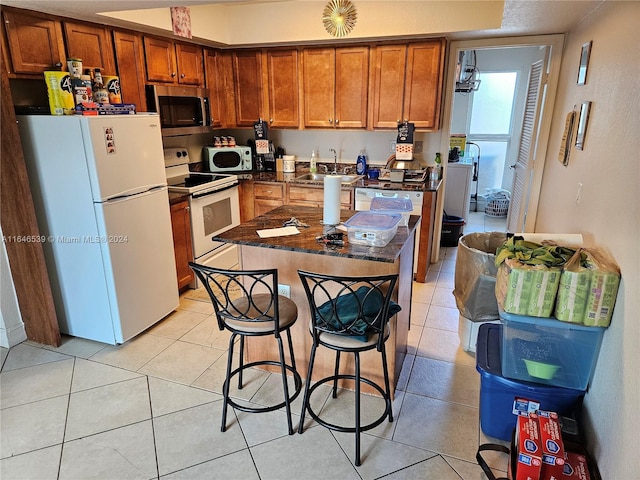 kitchen featuring a center island, a kitchen bar, sink, light tile patterned floors, and white appliances