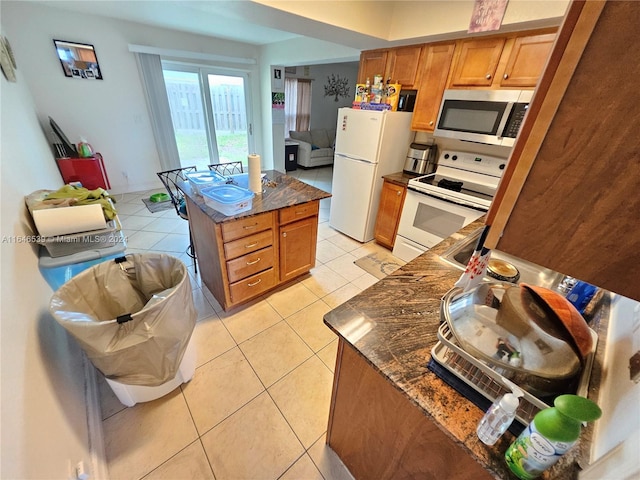 kitchen featuring dark stone counters, light tile patterned floors, a kitchen island, and white appliances