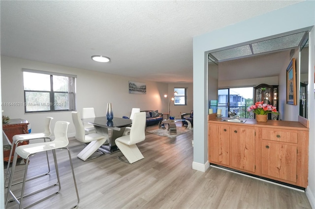 dining area with a textured ceiling, light wood-type flooring, and sink