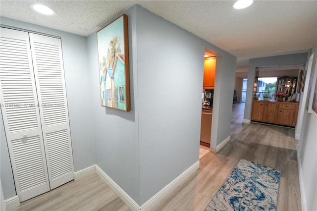 hall with a textured ceiling and light wood-type flooring