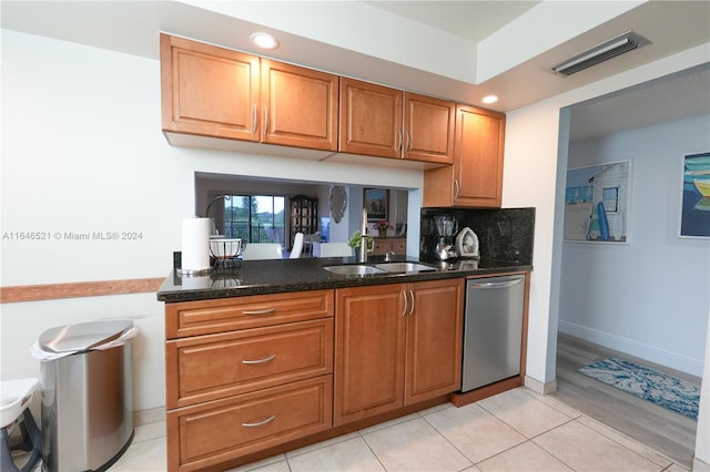 kitchen featuring light tile patterned floors, sink, stainless steel dishwasher, backsplash, and dark stone countertops