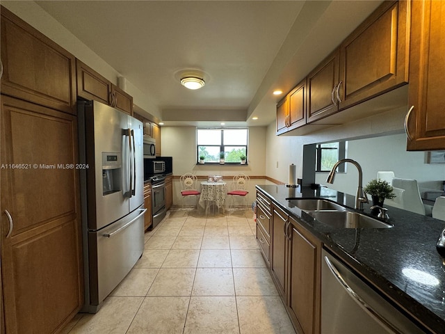 kitchen with dark stone counters, appliances with stainless steel finishes, light tile patterned floors, and sink