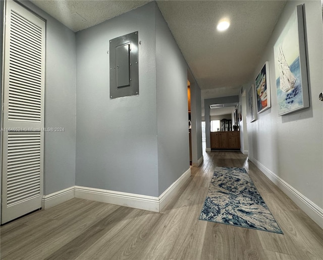 hall with light wood-type flooring, a textured ceiling, and electric panel