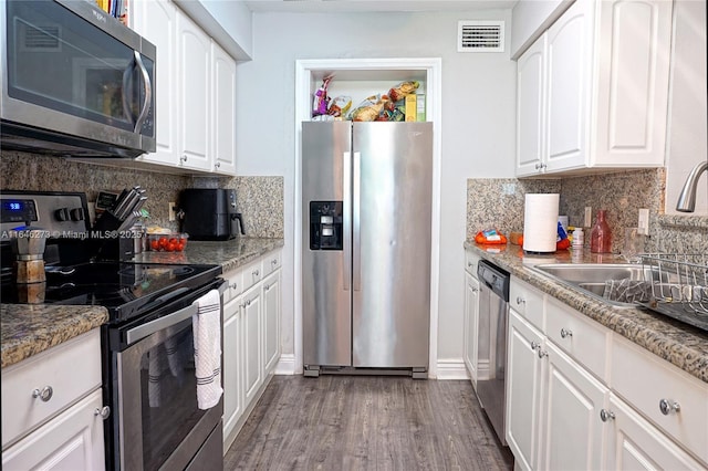 kitchen with appliances with stainless steel finishes, sink, white cabinets, light stone countertops, and dark wood-type flooring