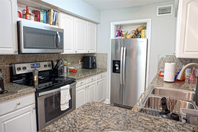 kitchen featuring tasteful backsplash, stainless steel appliances, dark stone countertops, and white cabinets