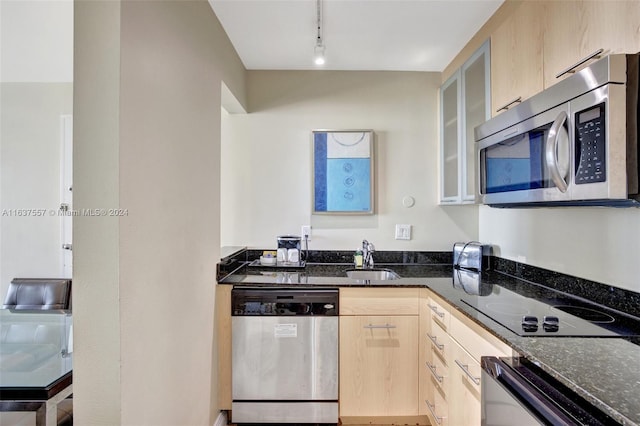 kitchen featuring light brown cabinetry, appliances with stainless steel finishes, dark stone countertops, and glass insert cabinets