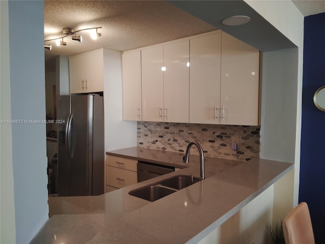 kitchen with white cabinets, sink, backsplash, and stainless steel fridge