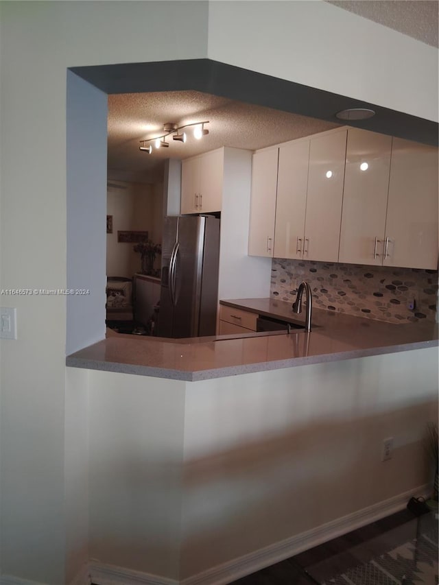 kitchen with white cabinetry, backsplash, a textured ceiling, stainless steel refrigerator with ice dispenser, and sink