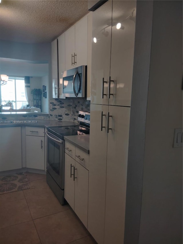 kitchen featuring tile patterned floors, appliances with stainless steel finishes, a textured ceiling, decorative backsplash, and white cabinets