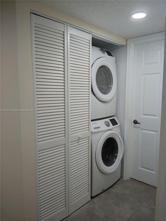 laundry area featuring stacked washer / drying machine, a textured ceiling, and tile patterned floors