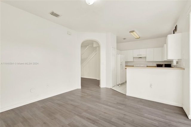 unfurnished living room featuring baseboards, visible vents, arched walkways, stairs, and light wood-type flooring