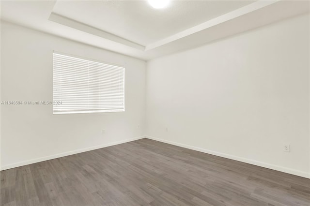 empty room with a raised ceiling, baseboards, and dark wood-style flooring