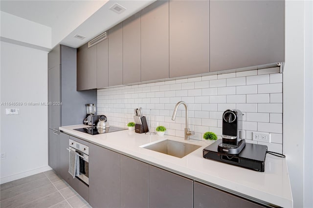 kitchen featuring black electric stovetop, oven, sink, gray cabinetry, and light tile patterned flooring