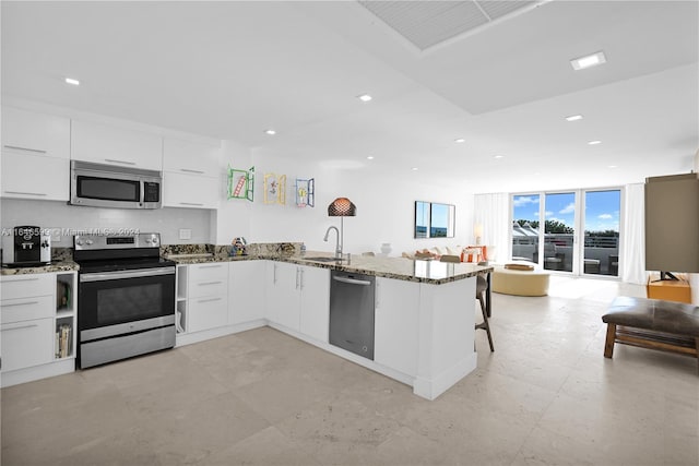 kitchen featuring stone countertops, kitchen peninsula, stainless steel appliances, sink, and white cabinets