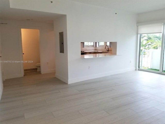 unfurnished living room featuring sink, light wood-type flooring, and electric panel