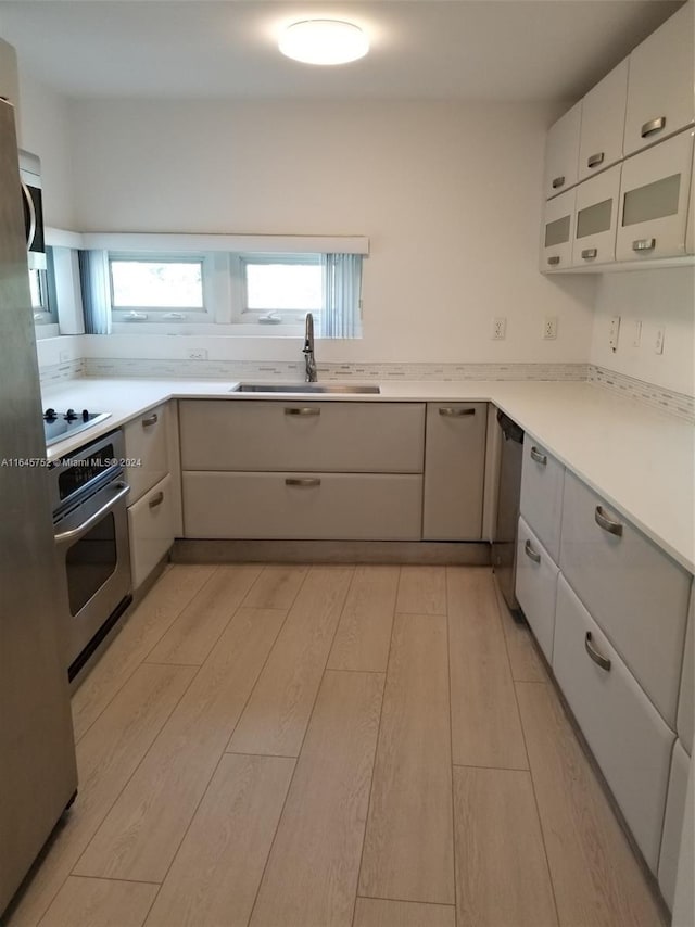 kitchen featuring sink, light hardwood / wood-style flooring, appliances with stainless steel finishes, and gray cabinets