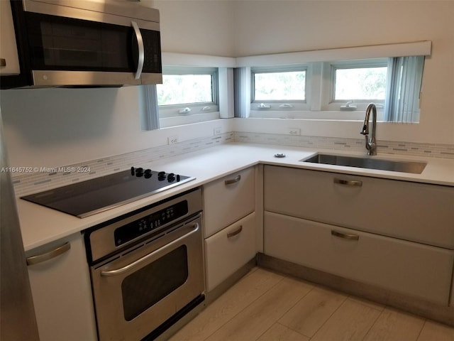 kitchen with appliances with stainless steel finishes, light wood-type flooring, sink, and tasteful backsplash