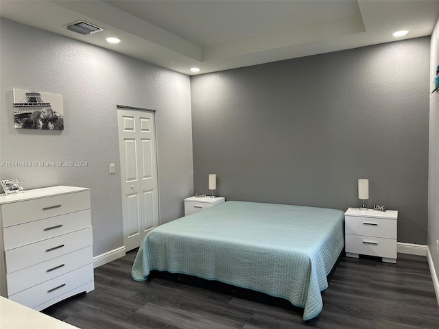 bedroom with dark hardwood / wood-style flooring, a closet, and a raised ceiling