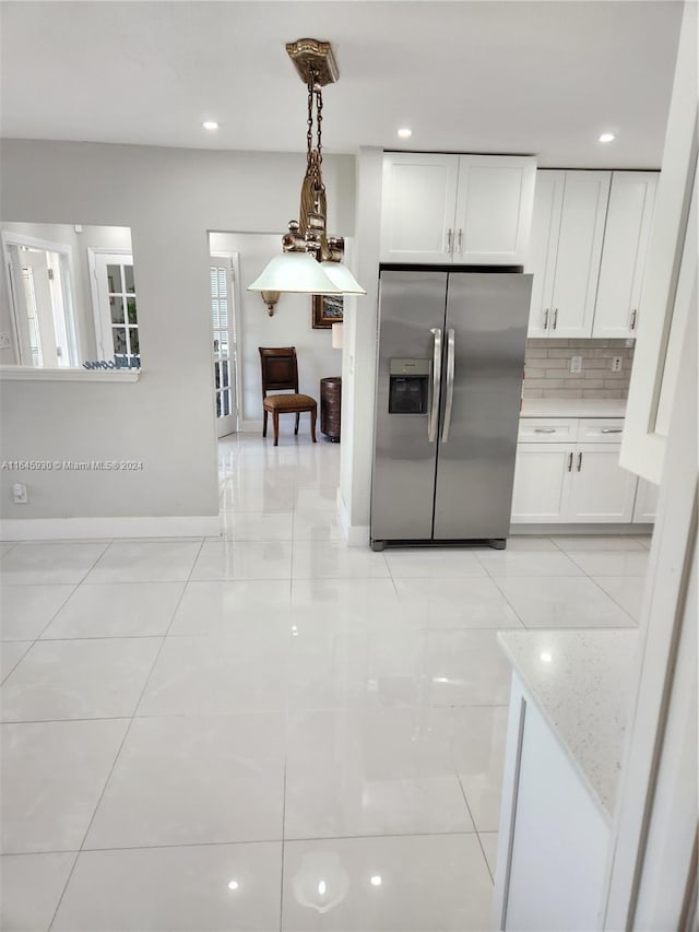 kitchen with backsplash, hanging light fixtures, stainless steel fridge, light stone counters, and white cabinetry