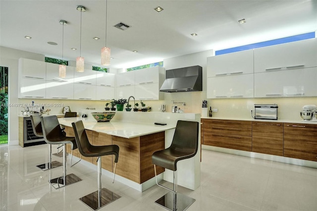 kitchen featuring a breakfast bar area, white cabinetry, wall chimney exhaust hood, and pendant lighting