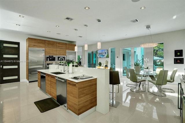 kitchen featuring stainless steel appliances, a kitchen island with sink, sink, decorative light fixtures, and light tile patterned flooring