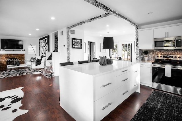 kitchen featuring appliances with stainless steel finishes, backsplash, dark hardwood / wood-style floors, a fireplace, and white cabinets