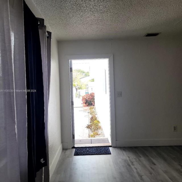 entryway with visible vents, a textured ceiling, baseboards, and wood finished floors