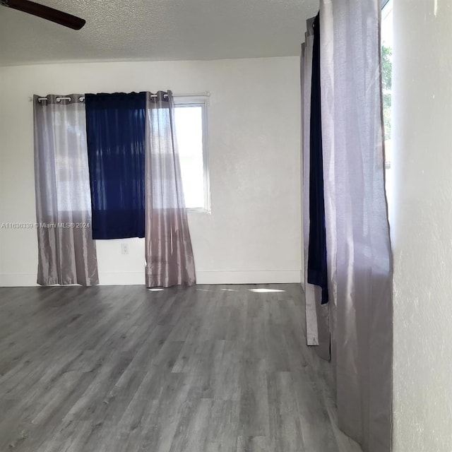 empty room featuring a textured ceiling, wood finished floors, and baseboards