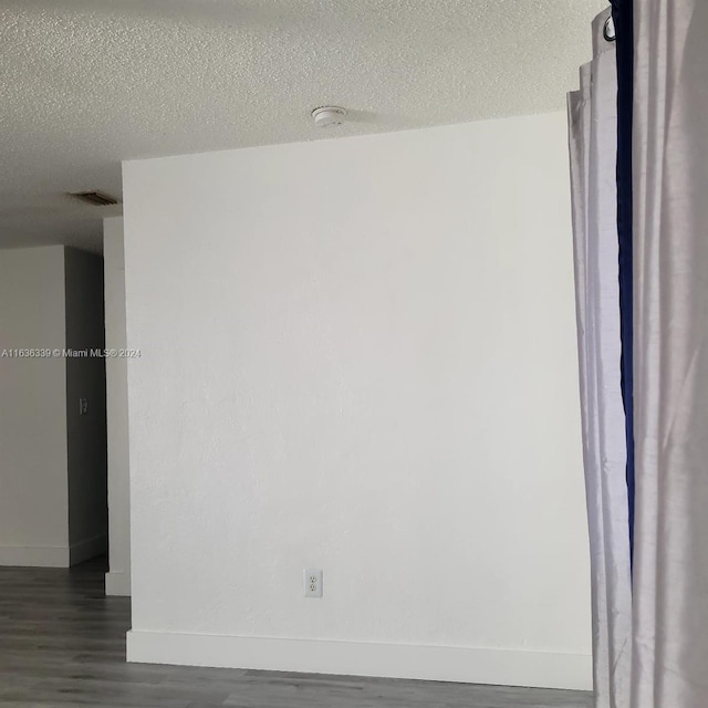 spare room featuring visible vents, baseboards, dark wood-type flooring, and a textured ceiling