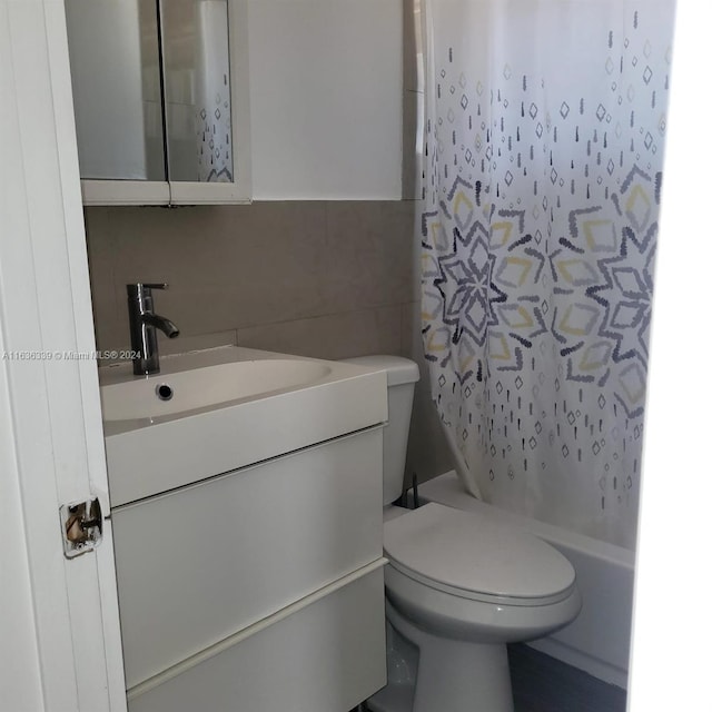 bathroom with toilet, shower / bath combo with shower curtain, vanity, and tile walls