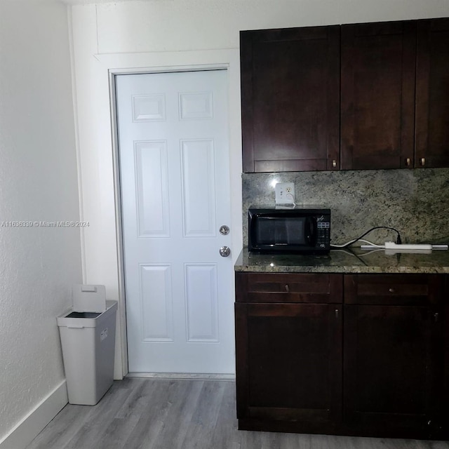 kitchen with black microwave, dark brown cabinetry, light wood-style floors, decorative backsplash, and dark stone counters