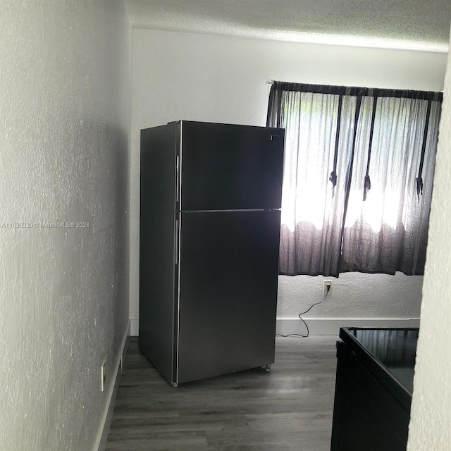 interior space with freestanding refrigerator, a textured wall, a textured ceiling, and wood finished floors